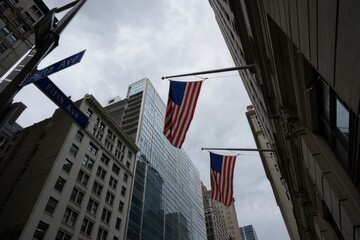 View looking up at tall city buildings with American flags flying on flagpoles against a cloudy sky at the intersection of Fifth Avenue