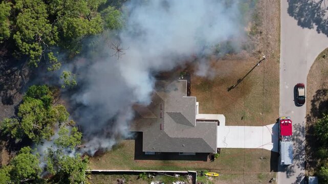 Smoke rises from a vegetation fire near suburban homes in Florida, as firefighters deploy hoses and fire trucks block the burning area