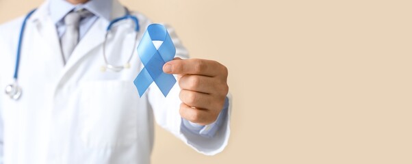 Male urologist holding blue ribbon on beige background with space for text, closeup. Prostate...