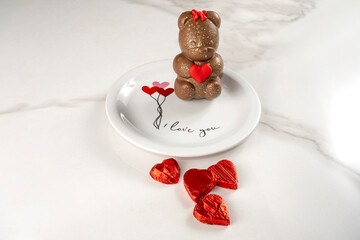 Chocolate teddy bear holding a heart next to heart shaped chocolates.