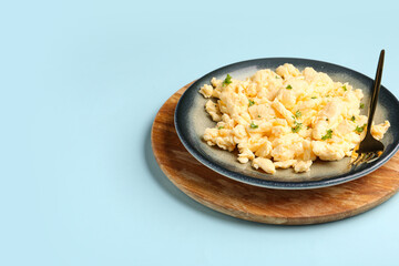 Plate of scrambled eggs with herbs on light blue background