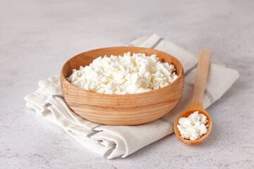 Bowl and spoon with tasty cottage cheese on light grunge background