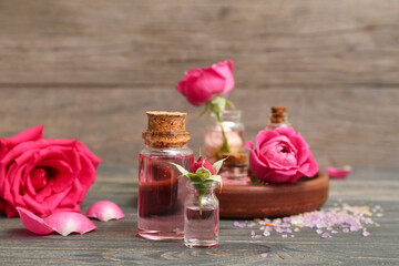 Bottles of cosmetic oil with rose extract and flowers on wooden table