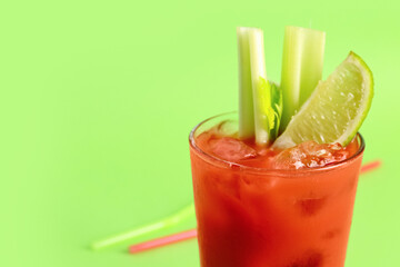 Glass of bloody mary with celery and lime on green background