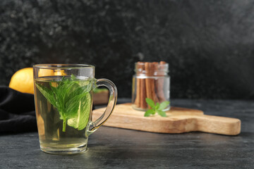 Wooden board with cup of fresh mint tea, lemons and cinnamon on grunge black table