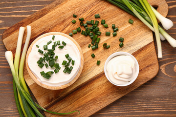 Bowls of tasty sour cream with sliced green onion on wooden background