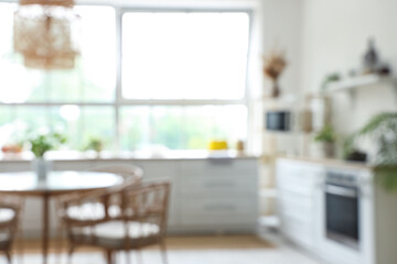 Interior of light kitchen with white counters, dining table and big window, blurred view