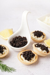 Tasty tartlets with black caviar on light background