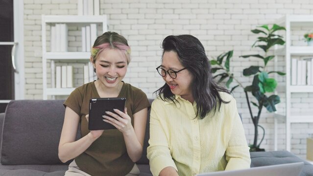Asian mother and daughter happily using tablet computer while sitting on sofa.