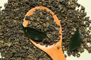 Wooden spoon with dry tea leaves on green background