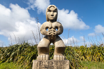 A powerful Maori carving, representing cultural heritage, stands among native New Zealand flax...