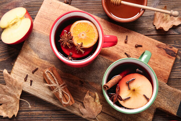 Cups of hot mulled wine with apple and orange on wooden background