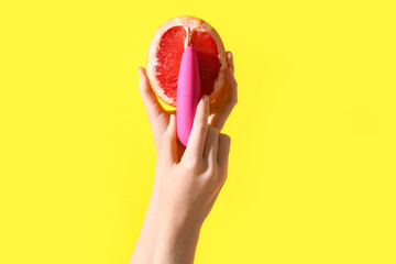Female hands with grapefruit and vibrator on yellow background. Sex education concept