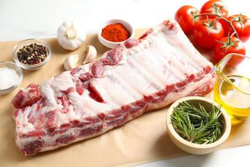 Raw pork ribs, spices and tomatoes on white table, closeup