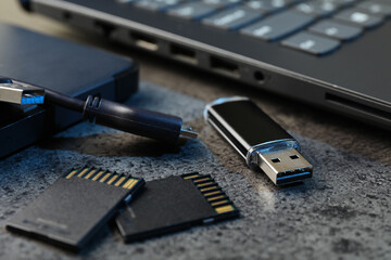 SD memory cards, USB flash drive, hard disk drive with cable and laptop on dark grey table, closeup