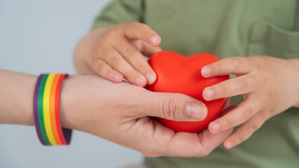 A faceless woman with a rainbow armband and her son hold a heart. 