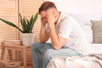 Young man suffering from headache in bedroom