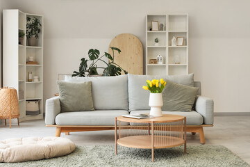 Obraz premium Modern interior of light living room with cozy sofa and coffee table with tulips