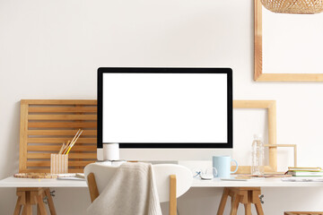 Workplace with modern computer and paint brushes near white wall in office