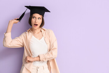 Funny female student in graduation hat on lilac background