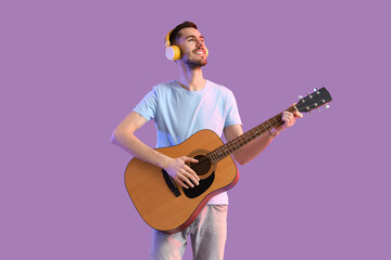 Obraz premium Young bearded man in headphones playing guitar on lilac background
