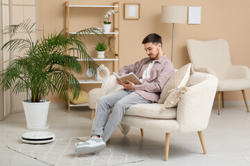 Modern robot vacuum cleaner near sofa with resting young man at home