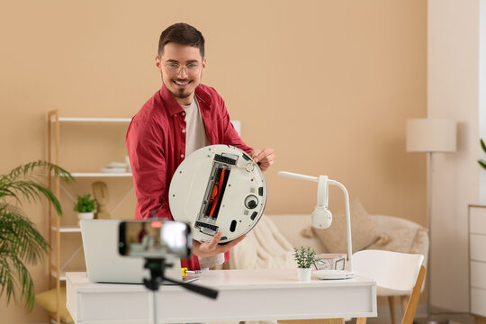 Young male blogger recording robot vacuum cleaner fixing tutorial at home