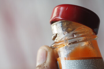 Close up of a glass bottle with a red cap held in hand