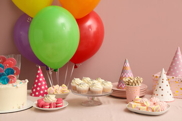 Table with different sweets and decor for birthday party against pink wall