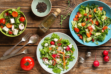 Bowls of fresh vegetable salad with radish and feta cheese on wooden background
