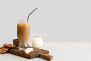 Glass of iced latte with sweet cookies and jug of milk on white background