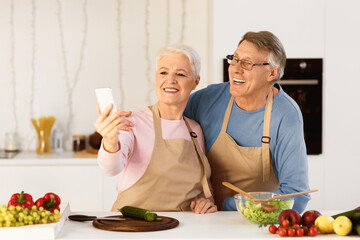 Joyful Elderly Spouses Making Selfie On Mobile Phone Having Fun Cooking Together Standing In Kitchen At Home. Modern Retirement Lifestyle, Senior People Using Gadgets And Enjoying Life Concept