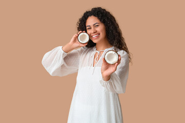 Beautiful young African-American woman with halves of fresh coconut on brown background