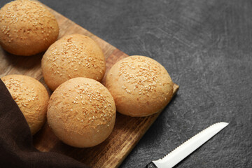 Wooden board of fresh buns with sesame seeds on dark background