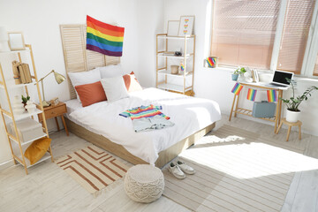 Interior of light bedroom with LGBT flags, workplace and shelf units