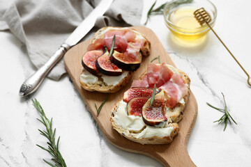 Wooden board of delicious fig bruschetta with prosciutto and ricotta cheese on white background, closeup