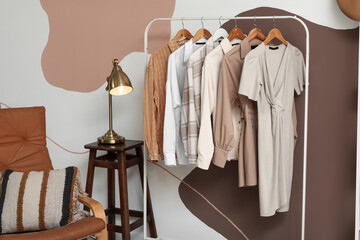Rack with clothes, shelving unit and lamp on stool near colorful wall in dressing room