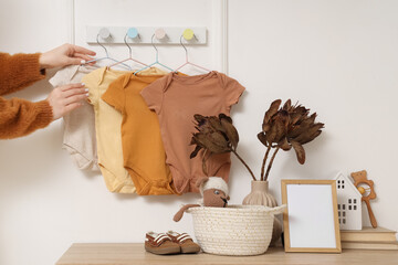 Female hands and rack with baby bodysuits on light wall at home
