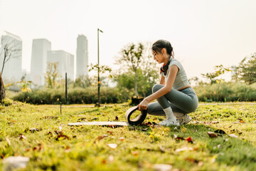 A woman dressed in workout clothes is spreading out a yoga mat to prepare for exercising at the park