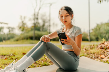 A woman dressed for exercise holds her phone and tracks her heart rate with a smartwatch as she sits on a yoga mat. Fitness and workout concept.