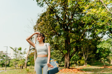 A woman is walking along a paved path in a green urban park, dressed in athletic wear including...