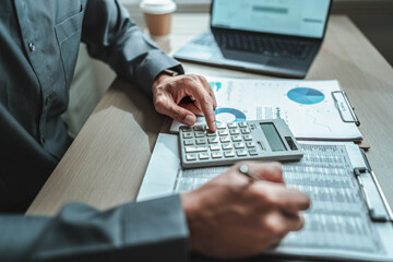 An accountant is seated at a desk in the office, utilizing a calculator to determine balances, profits, currency conversions, and costs. This involves various accounting and financial concepts.