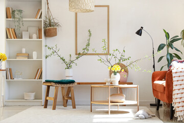 Interior of light living room with bookshelf, daffodils and blossoming branches in vases