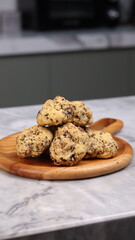 A close-up image of a pile of rustic-style chocolate chip cookies placed on a round wooden serving plate with a handle. The cookies have a homemade, chunky appearance with visible chocolate chunks and