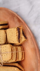 A close-up of handmade chocolate sandwich cookies tied with rustic twine, neatly stacked on a wooden plate. The golden brown biscuits with rich chocolate filling evoke a warm, homemade feel. Styled in