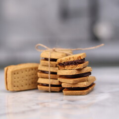 A close-up of handmade chocolate sandwich cookies tied with rustic twine, neatly stacked on a wooden plate. The golden brown biscuits with rich chocolate filling evoke a warm, homemade feel. Styled in