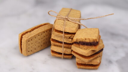 A close-up of handmade chocolate sandwich cookies tied with rustic twine, neatly stacked on a wooden plate. The golden brown biscuits with rich chocolate filling evoke a warm, homemade feel. Styled in