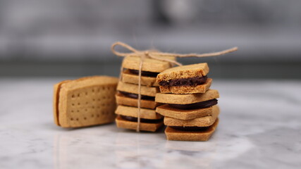 A close-up of handmade chocolate sandwich cookies tied with rustic twine, neatly stacked on a wooden plate. The golden brown biscuits with rich chocolate filling evoke a warm, homemade feel. Styled in