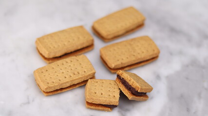 A close-up of handmade chocolate sandwich cookies tied with rustic twine, neatly stacked on a wooden plate. The golden brown biscuits with rich chocolate filling evoke a warm, homemade feel. Styled in