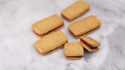 A close-up of handmade chocolate sandwich cookies tied with rustic twine, neatly stacked on a wooden plate. The golden brown biscuits with rich chocolate filling evoke a warm, homemade feel. Styled in